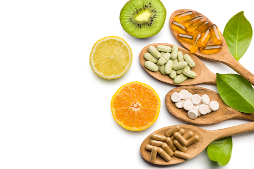 photo showing several types of vitamin supplements alongside a slice of kiwi, lemon, and orange.