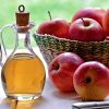 Bottle of Apple cider vinegar sitting on table with several red apples.