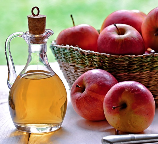 Bottle of Apple cider vinegar sitting on table with several red apples.