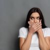 woman covering mouth with both hands looking to her left.