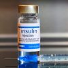 Bottle of insulin with hypodermic needle laying next to it.