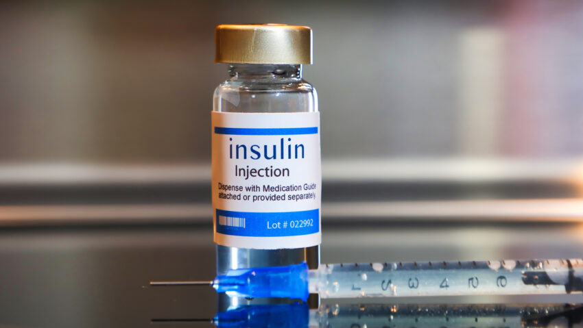 Bottle of insulin with hypodermic needle laying next to it.